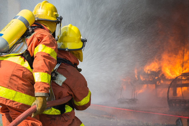 2 bombeiros pulverizando água na operação de combate a incêndios
 - Foto, Imagem