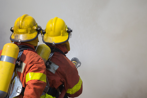 2 Feuerwehrleute versprühen Wasser in Feuer und Rauch  - Foto, Bild