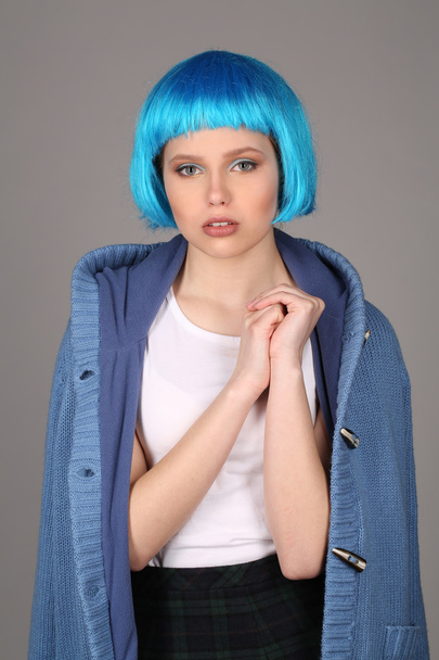 Girl in blue wig and coat compressing her arm. Close up. Gray background - Foto, Imagem