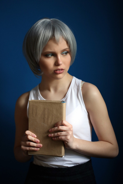 Girl in silver wig posing with book. Close up. Blue background - 写真・画像