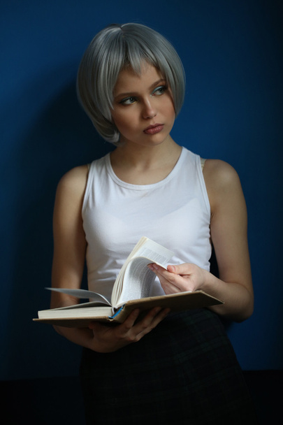 Teen with silver hair leafing through the book. Close up. Blue background - Фото, зображення