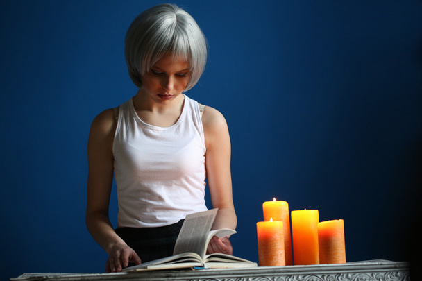 Teenie-Model posiert mit Buch und Kerzen. Nahaufnahme. blauer Hintergrund - Foto, Bild