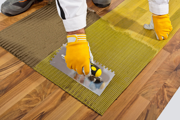 Applica adesivo per piastrelle sul pavimento in legno con rinforzo in fibra di maglia
 - Foto, immagini