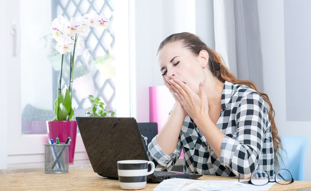 Tired woman yawning during working in home office using laptop - 写真・画像