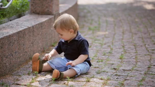 Un garçon d'un an est assis sur un bloc de pierre dans le parc. Jour d'été
. - Séquence, vidéo