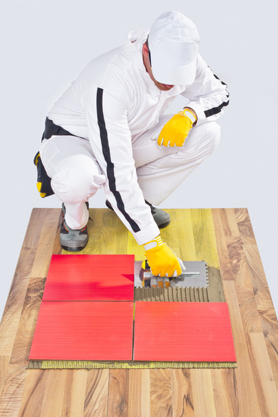 Trabajador aplica baldosas cerámicas en suelo de madera con llana con muescas
 - Foto, imagen