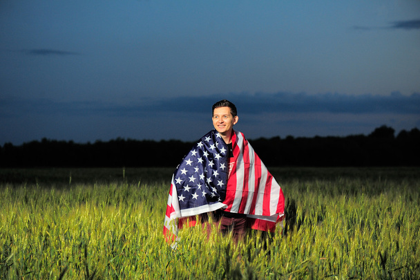 Χαμογελαστός άνθρωπος σε έναν τομέα σίτου με αμερικανική σημαία - Φωτογραφία, εικόνα
