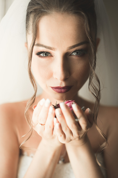 Beautiful young bride with makeup and hairstyle in bedroom, newlywed woman final preparation for wedding. Happy girl waiting groom. Portrait soft focus - Photo, image