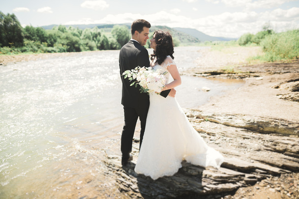 Elegant stylish happy brunette bride and gorgeous groom on the background of a beautiful waterfall in the mountains - Foto, Imagen
