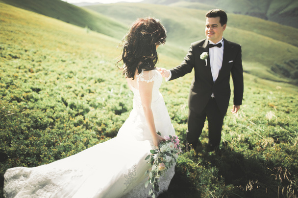 Όμορφη πανέμορφη νύφη ποζάρει στον γαμπρό και διασκεδάζει, πολυτελή τελετή στα βουνά με καταπληκτική θέα, χώρος για κείμενο, γαμήλιο ζευγάρι - Φωτογραφία, εικόνα