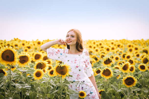 mooie zoete sexy meisje in een witte jurk lopen op een veld met zonnebloemen, glimlachend een mooie glimlach, vrolijke meisje, style, lifestyle, ideaal voor reclame en foto zon schijnt fel en sappig - Foto, afbeelding