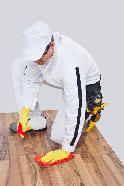 werknemer reinigt met handdoek en spray houten vloer voordat tilling - Foto, afbeelding