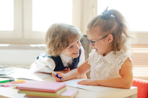 Two little classmate, laddie and girlie, are sitting at the same desk. - Foto, Imagen