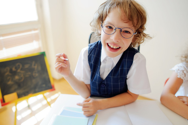 Funny little schoolboy in glasses sits at a school desk. - Photo, Image