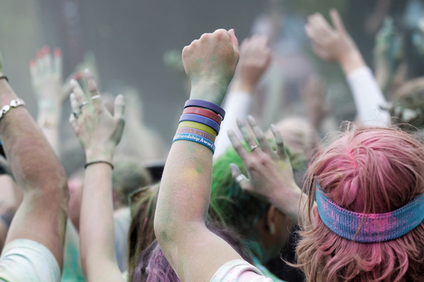 Щаслива аудиторія з руками в повітрі і кольоровий порошок в повітрі
 - Фото, зображення