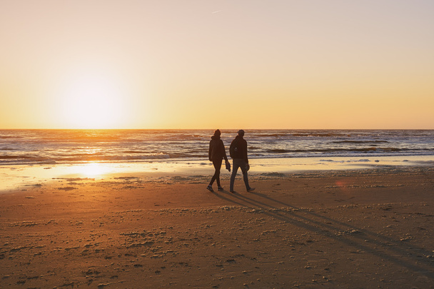 Люди прогуливаются по пляжу во время заката
. - Фото, изображение