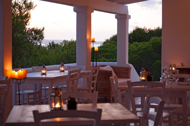 Formentera, Ilhas Baleares, Espanha: luzes suaves, mesas e velas para um jantar romântico com vista panorâmica do Mar Mediterrâneo e maquis visto do terraço branco de um restaurante
  - Foto, Imagem