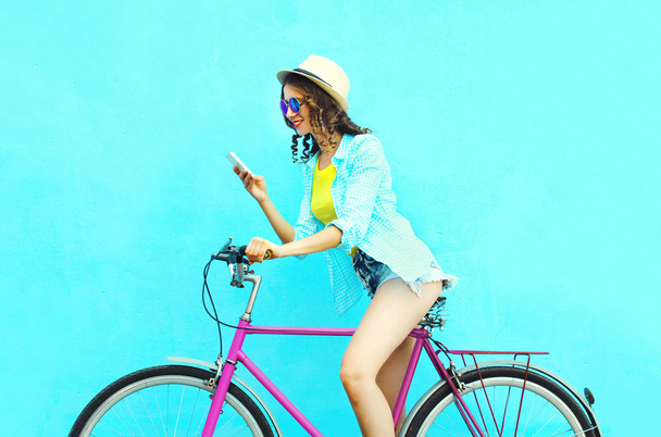 Pretty cool smiling woman using smartphone on retro bicycle over - Фото, изображение