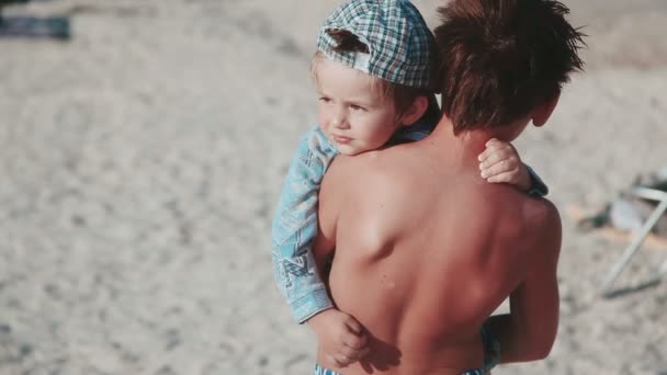 Twee broers. De oudste broer houdt zijn jongere broer in zijn armen op het strand. Een familie. - Video