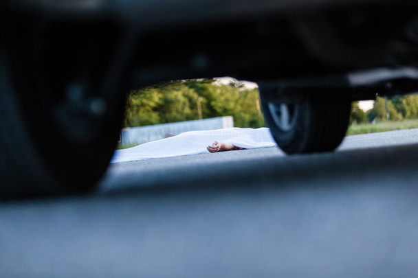 Dode lichaam bedekt met blad met auto in de buurt - Foto, afbeelding