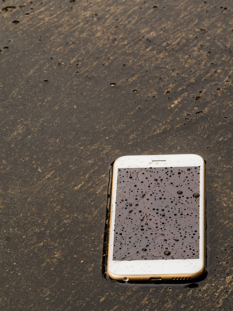 Teléfono inteligente mojado caído en el suelo de inundación
 - Foto, Imagen