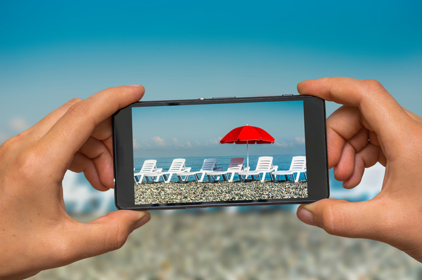 Telefon ile güneşlenme yatakları ve kırmızı şemsiye fotoğraf çekme - Fotoğraf, Görsel