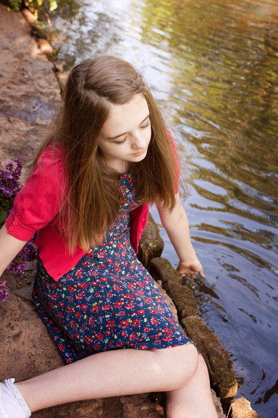 Όμορφο εφηβικό κορίτσι που κάθεται δίπλα σε ένα ποτάμι - Φωτογραφία, εικόνα
