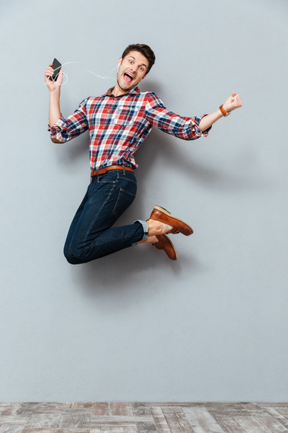 Happy man listening to music from cell phone and jumping - 写真・画像