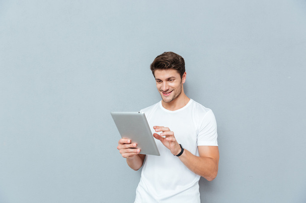 Happy attractive young man standing and using tablet - Fotoğraf, Görsel
