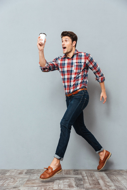 Attractive young man holding cup of takeaway coffee and running - Zdjęcie, obraz