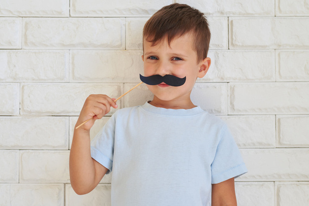 Young gentleman holding paper moustache with rather shrewd look - Photo, Image