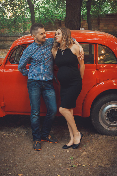 Man and pregnant woman near red car - Foto, Imagen