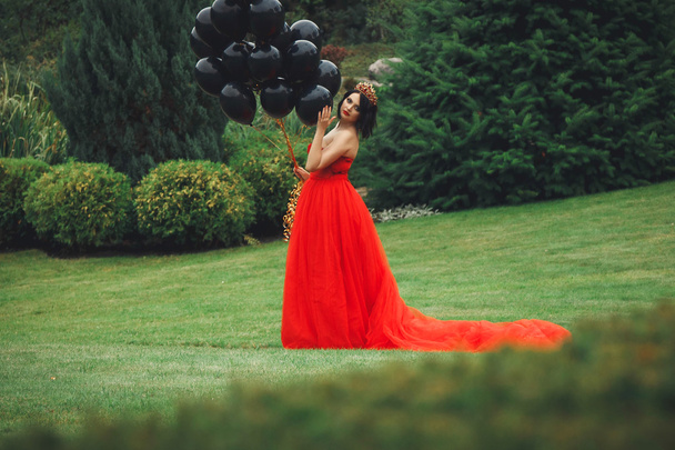 hinreißende Frau im roten Kleid mit schwarzen Luftballons - Foto, Bild
