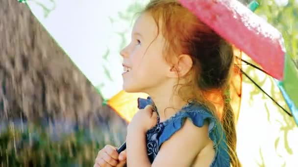 Portrait in profile of a carefree girl who enjoys the rain. It should be under the umbrella of the rainbow color - Séquence, vidéo