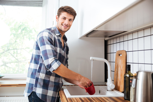 Happy young man standing and washing dishes on the kitchen - Foto, Bild