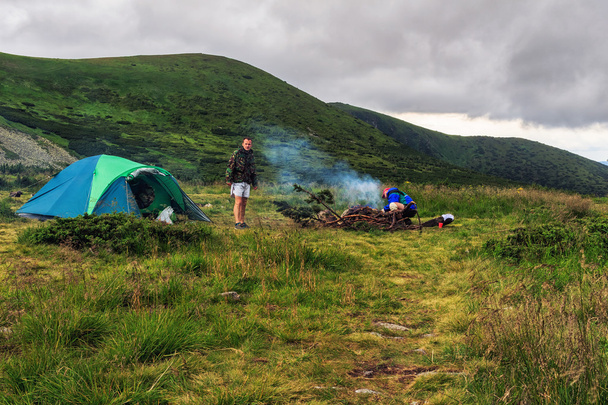 Camping tent and two men tourists at campfire in Carpathian mountains, summertime journey. - Photo, Image