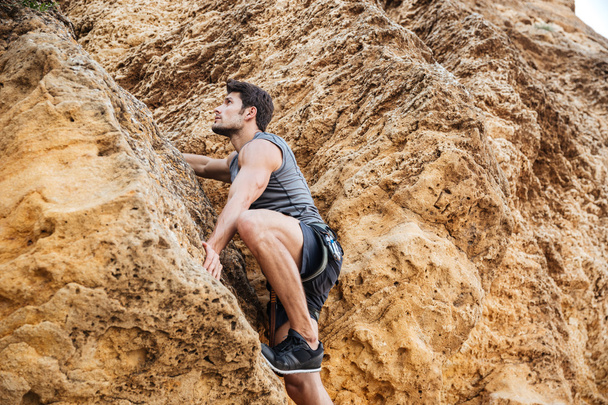 Young man climbing natural rocky wall - Foto, afbeelding