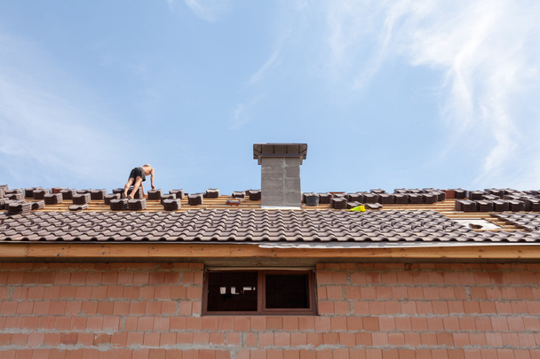 Dakbedekking: bouwvakker op een dak bedekken met tegels - dak renovatie: installatie van teer papier, nieuwe tegels en schoorsteen - Foto, afbeelding