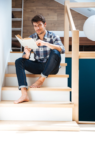 Young handsome man reading book while sitting on the stairs - Foto, afbeelding