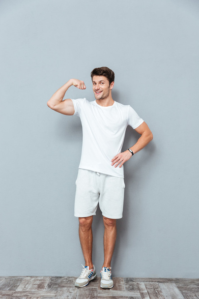 Full length of happy athletic man standing and showing biceps - Foto, Bild