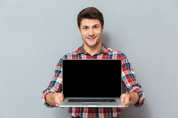 Smiling young man in checkered shirt holding blank screen laptop - Foto, Imagen