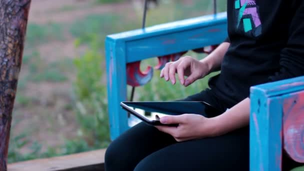 Το κορίτσι με το tablet σε μια ξύλινη ταλάντευση χέρια - Πλάνα, βίντεο