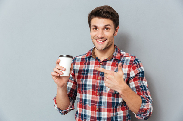 Young handsome smiling man pointing finger at takeaway coffee cup - Foto, immagini