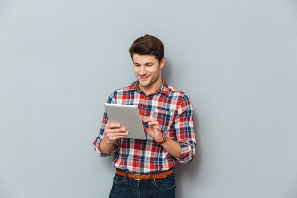 Happy young man in plaid shirt standing and using tablet - Foto, immagini