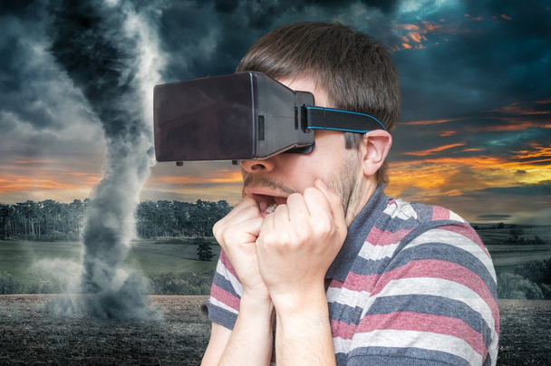 3D simulation concept. Man is wearing virtual reality headset and is scared from tornado and storm. - Photo, Image