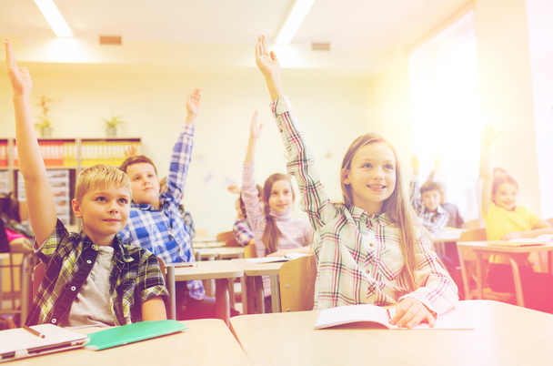 group of school kids raising hands in classroom - Zdjęcie, obraz