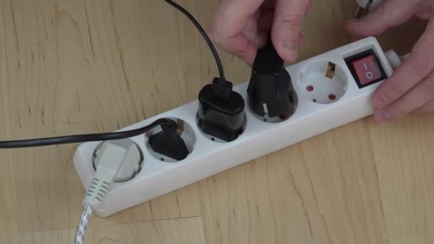 man hands insert wire plugs and turn on extension switch on wooden floor. - Footage, Video