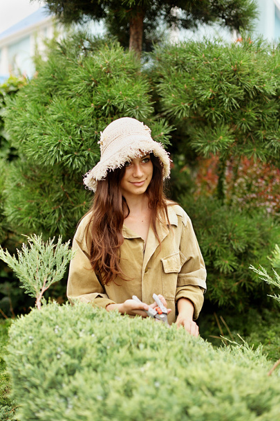 Chica jardinero en ropa de trabajo y sombrero de paja corta tijeras de jardín siempreverde
 - Foto, imagen