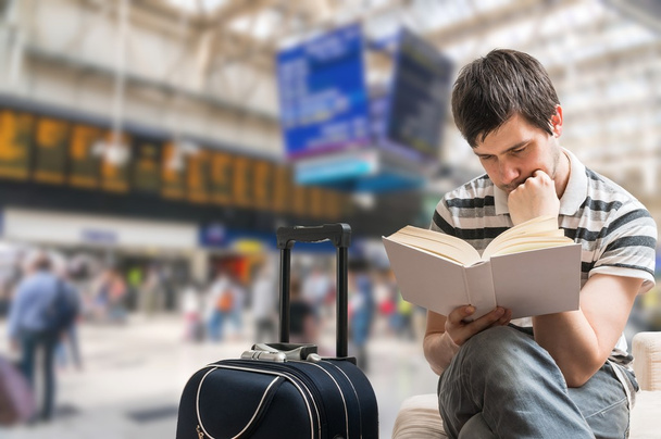 Delayed train concept. Passenger is sitting in train station, reading book and waiting for train arrival. - Photo, Image