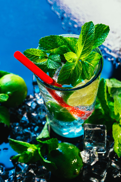 glass of mojito with lime and mint ice cube close-up red straw on blue background - Foto, afbeelding